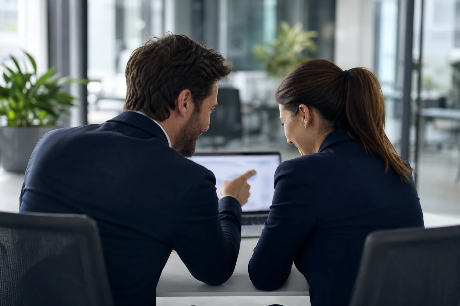 Two colleagues finding an answer together at a laptop in a bright office